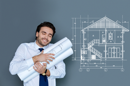 Happy architect. Cheerful emotional professional architect standing with a bunch of schemes in his hands and kindly smilingの写真素材