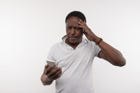 Digital age. Pleasant nice man touching his head while holding a smartphone in his handsの写真素材