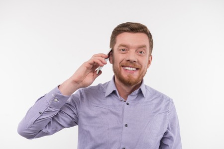 Distance communication. Happy bearded man putting a phone to his ear while making a callの写真素材