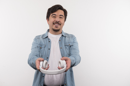 Try it. Joyful nice man holding his headphones while giving it to youの写真素材