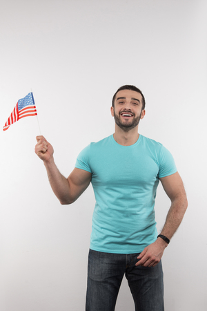 American patriot. Delighted nice man holding a US flag while looking at youの写真素材