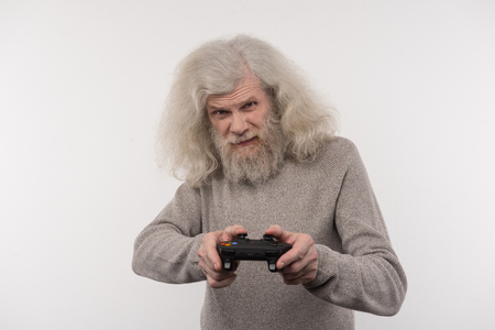 New technology. Pleasant aged man standing against white background while playing gamesの写真素材