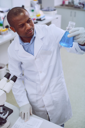 Good work. Concentrated smart biologist wearing a uniform and holding a tubeの写真素材