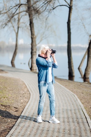 I like photographing. Concentrated mature woman taking pictures while walking in the parkの写真素材
