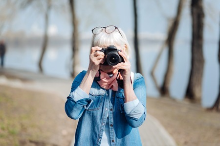My favourite activity. Inspired mature woman taking pictures while walking in the parkの写真素材