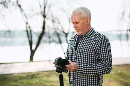Real photography. Concentrated senior man looking down and using cameraの写真素材