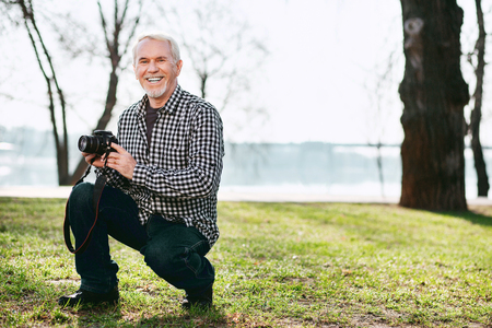 Photo session. Cheerful senior man grinning and using cameraの写真素材
