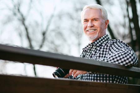 First photo. Low angle of positive mature man utilizing camera and smiling to cameraの写真素材