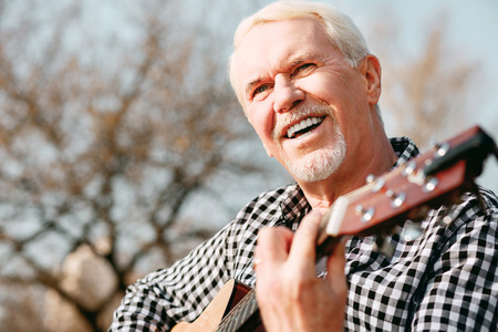 Mental health. Low angle of merry mature man laughing and enjoying guitar playの写真素材