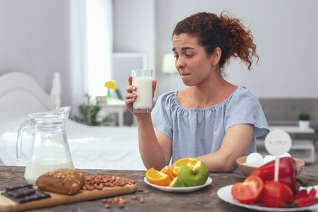 Staying healthy. Young girl sitting at a dinner table trying to consume her daily ratio of calcium by drinking a glass of milk every dayの写真素材
