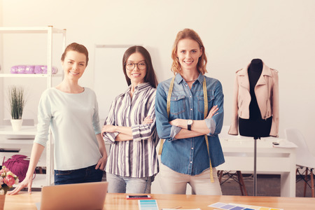 Choose us. Team of confident professional tailors putting arms together while standing in front of you and smilingの写真素材