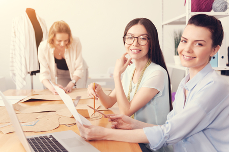 Always diligent. Close up of positive successful designers holding sewing pattern and pencils while smiling at youの写真素材