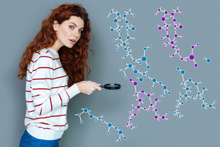 Studying chemistry. Beautiful long haired student looking interested and holding a magnifying glass...