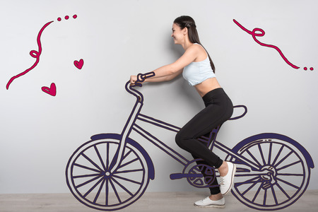 Riding a bike. Cheerful sporty student leading a healthy lifestyle and riding a bike