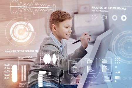 Smart child. Cheerful clever child sitting with a stylus and pointing to the screen of his modern computerの写真素材