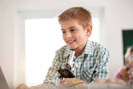 Pleasurable activity. Delighted blonde boy smiling while enjoying his schoolworkの写真素材