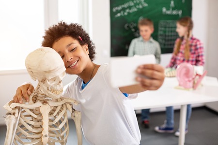 Joyful mood. Positive delighted boy standing near the skeleton while trying to take a selfieの写真素材