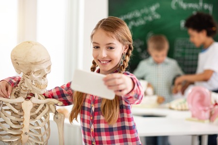 Happy smile. Cheerful positive girl smiling into the camera while taking a selfie with the skeletonの写真素材