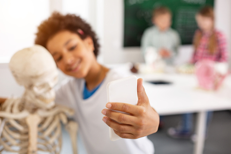 Selfie time. Selective focus of a white smartphone being in hands of a cheerful happy boyの写真素材