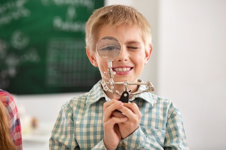Laboratory equipment. Cheerful nice boy looking into the magnifying glass while being in the school labの写真素材