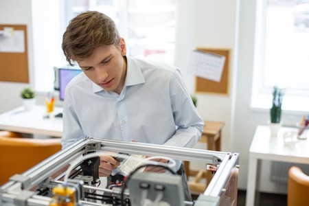 Correct data. Charming young man figuring out parameters of a model made with a 3D printer while...