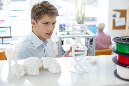 Admiring high quality. Charming young man examining a 3D atom model made with a 3D printer, having taken it from the shelfの写真素材