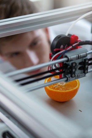 Future is here. The top view of a 3D printer creating a model of an orange while the young engineer monitoring the processの写真素材