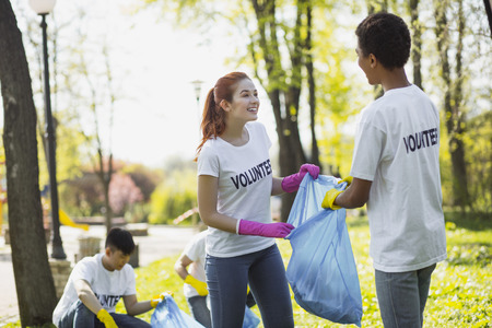 Volunteer for country. Cheerful two volunteers holding garbage bag and staring at each otherの写真素材