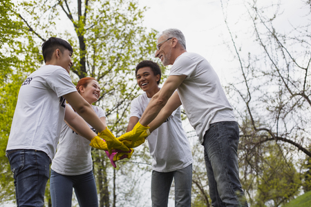 Team spirit. Low angle of optimistic vigorous volunteers standing and holding hands togetherの写真素材