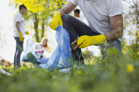 Become volunteer. Close up of male hands dressing in rubber gloves and using garbage bagの写真素材