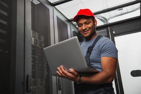 Effective IT system. Low angle of jolly IT engineer smiling and holding laptopの写真素材