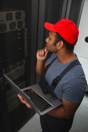 IT challenges. Top view of musing IT engineer touching chin and holding laptopの写真素材