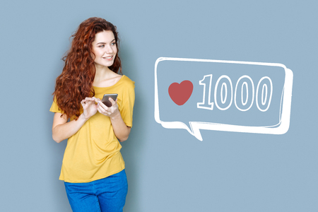 Popular blogger. Cheerful popular blogger looking glad while standing with a smartphone and checking...