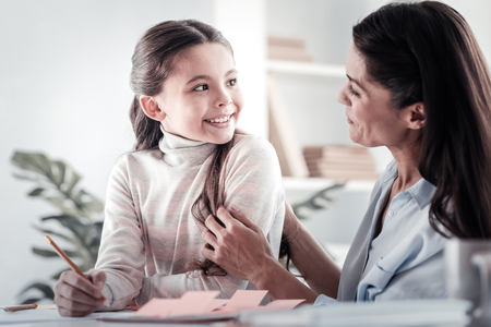 Keep smiling. Pretty little female sitting at her table while discussing task with her helperの写真素材
