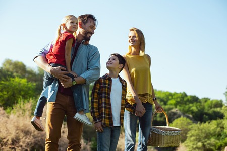Our kids. Cheerful dark-haired man holding his daughter while spending time with his familyの写真素材