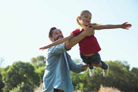 Happy childhood. Inspired bearded father smiling while having fun with his little daughterの写真素材