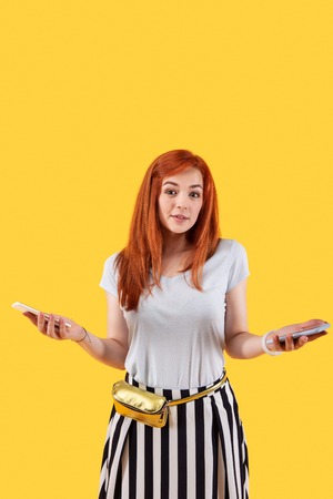 What to choose. Positive red haired woman looking at you while choosing between smartphones