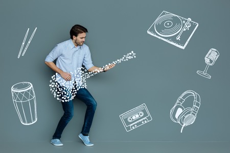 Playing the guitar. Positive expressive young musician looking concentrated while playing the guitarの写真素材
