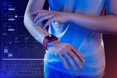 Smart watch. Responsible professional software developer standing in his futuristic office and testing a hologram on his new smart watchの写真素材