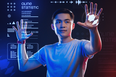 Controlling the situation. Calm attentive young man carefully touching the transparent screen and...