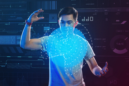 Making wide holograms. Calm clever student looking concentrated while standing in front of a transparent screen and making a hologramの写真素材