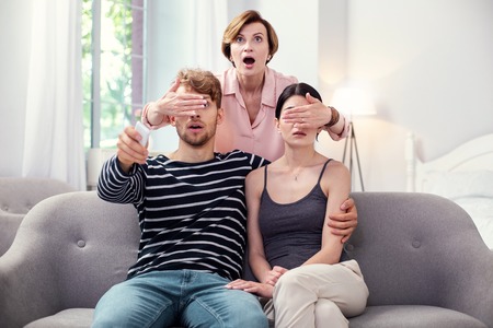 What are you watching. Pleasant emotional woman standing behind the couple and closing their eyes while controlling what they are watchingの写真素材