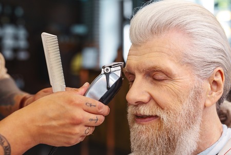 Final detail. Pleased bearded man keeping eyes closed while enjoying the process in salonの写真素材
