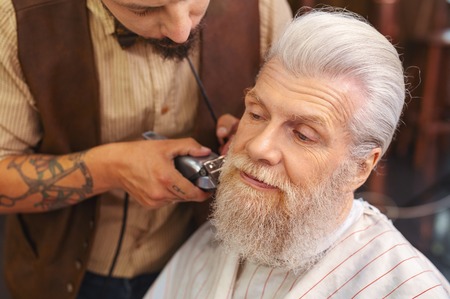 So surprised. Delighted bearded man wrinkling forehead while creating new form of his beardの写真素材