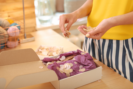 Nice decorations. Young beginning craftswoman feeling inspired while sprinkling package for clients with decorationsの写真素材