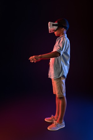Difficult game. Pleased afro-american boy wearing a VR headset and typing on a keyboardの写真素材