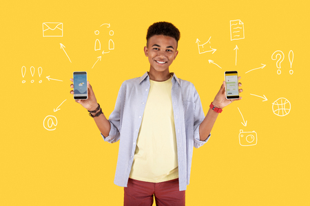Choosing a smartphone. Emotional cheerful student holding two modern smartphones and smiling while being in the shop and choosing the best deviceの写真素材