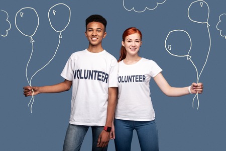 Beautiful balloons. Cheerful friendly volunteers feeling happy while being at the children party and holding beautiful balloonsの写真素材