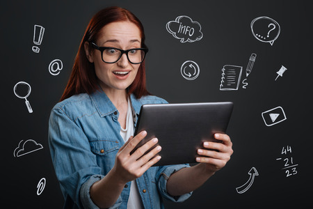 Amazing news. Emotional popular blogger looking at the screen of her modern tablet and feeling excited while seeing the number of followersの写真素材