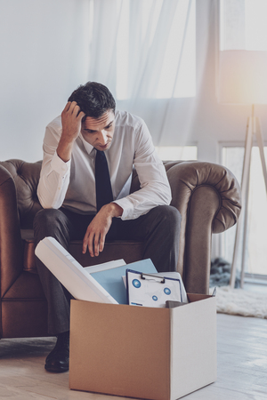 At loss. Sad depressed man looking at the box with his stuff while thinking what to doの写真素材
